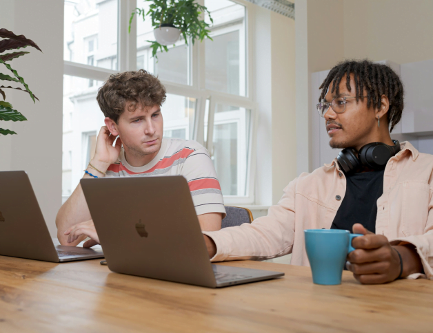 Deux jeunes hommes travaillant devant leurs ordinateurs et discutant.